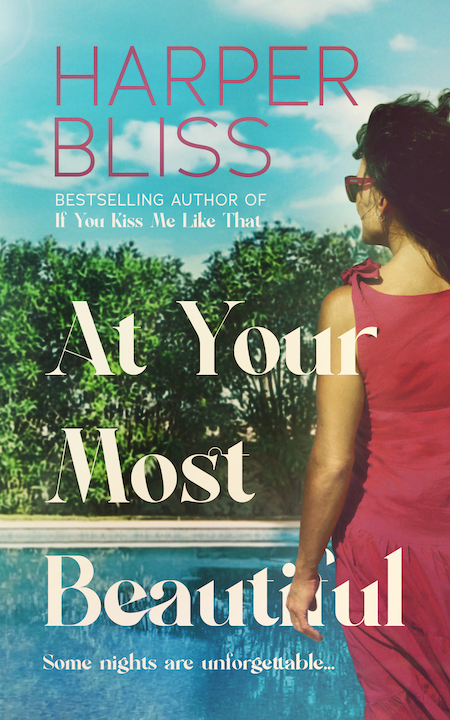 Book cover for 'At Your Most Beautiful' by Harper Bliss, featuring a woman in a red dress gazing at a pool with lush greenery in the background